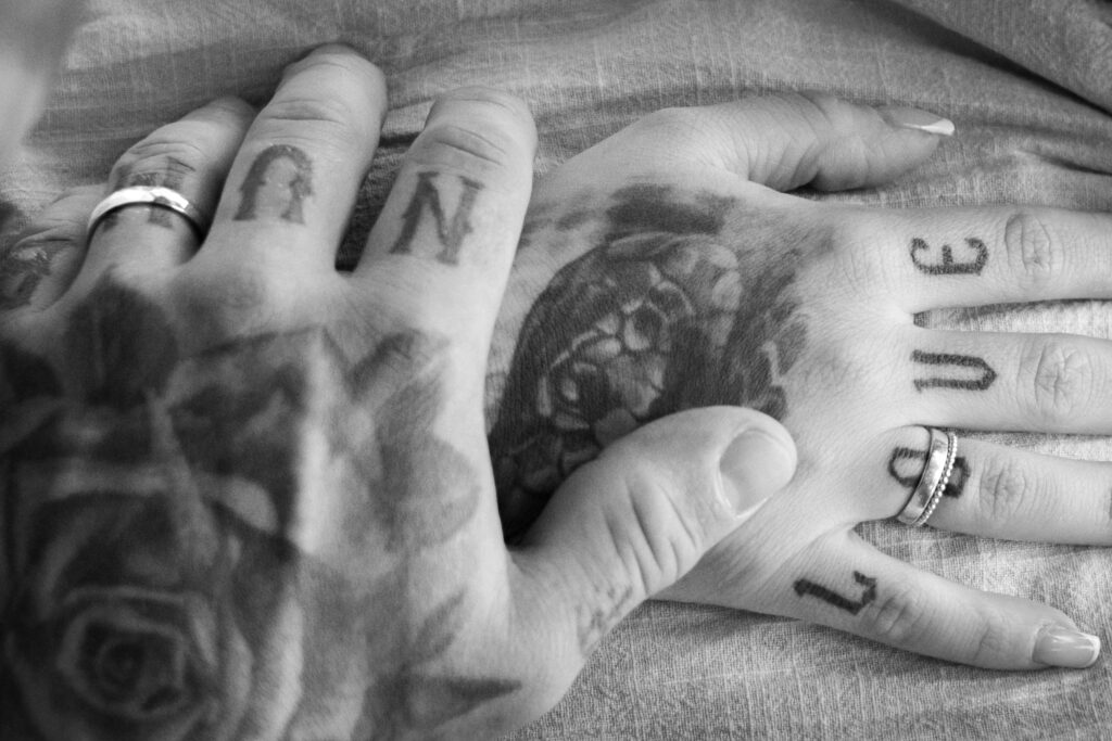Nahaufnahme von tattoowierten Händen mit Eheringen, schwarz-weiß